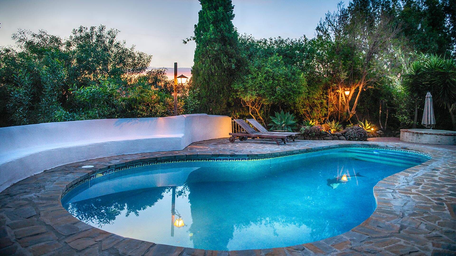 Rond zwembad omringd met steen en veel groen tijdens schemering