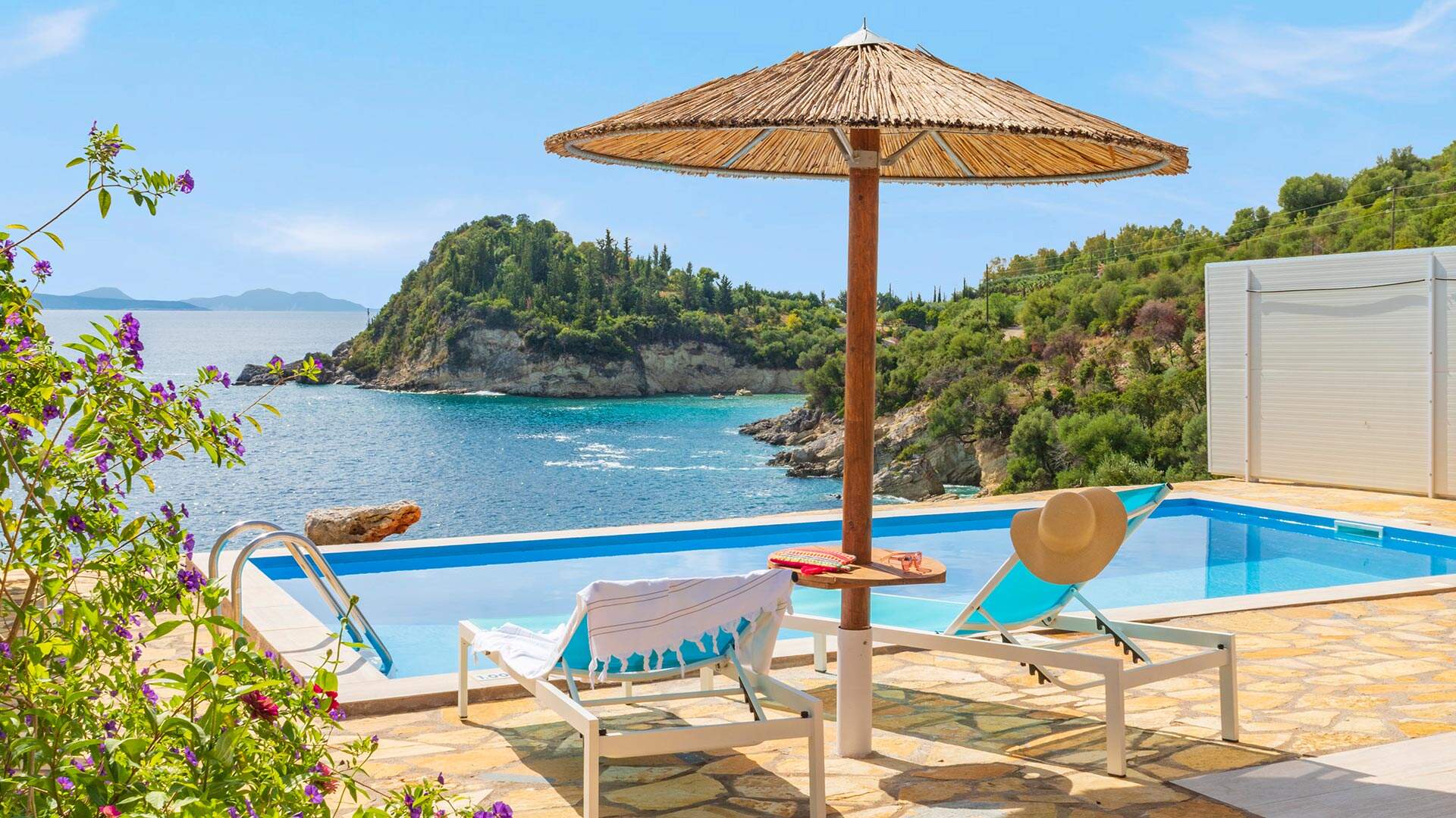 ligbedjes met rieten parasol aan infinity pool met uitzicht op zee 