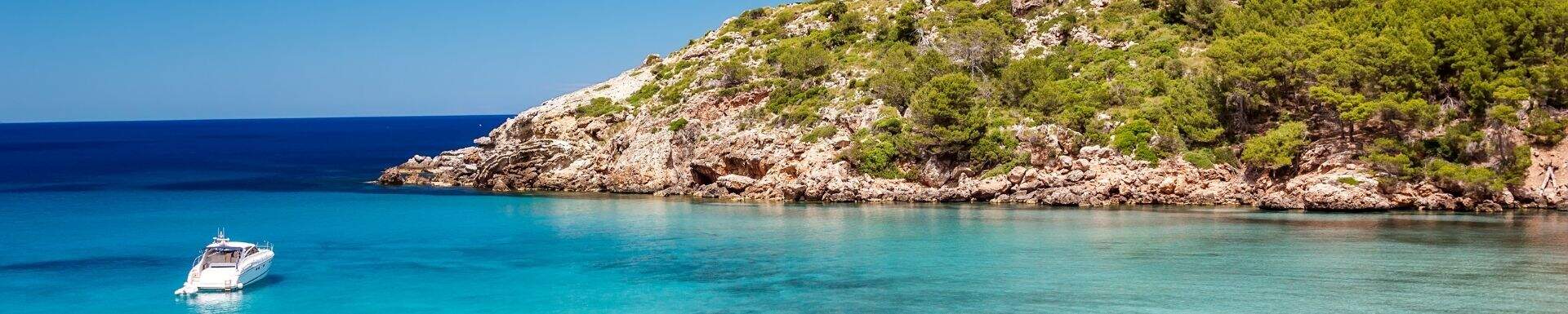 Groene kust van Menorca met een witte boot in het helderblauwe water