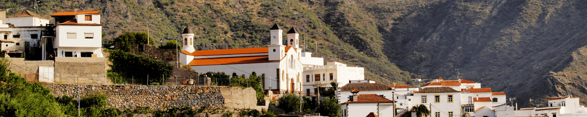 Pittoresk dorp op Gran Canaria met witte gebouwen en rode daken, gelegen tegen een bergachtig landschap.